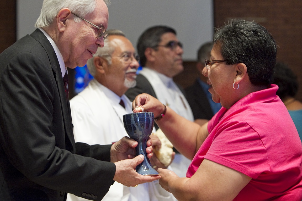 El Rdo. Noé Gonzales (izq.) le ofrece la Santa Comunión a Nohemi Ramirez durante el culto de adoración  en El Paso, Texas. Photo by Mike DuBose, Comunicaciones Metodistas Unidas.