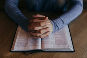 Image shows hands folded on pages of a Bible. Creative Commons, courtesy of Unsplash. 