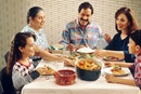 A Hispanic family (male adult, two female adults, female child, and male child) enjoy a meal at the dinner table.