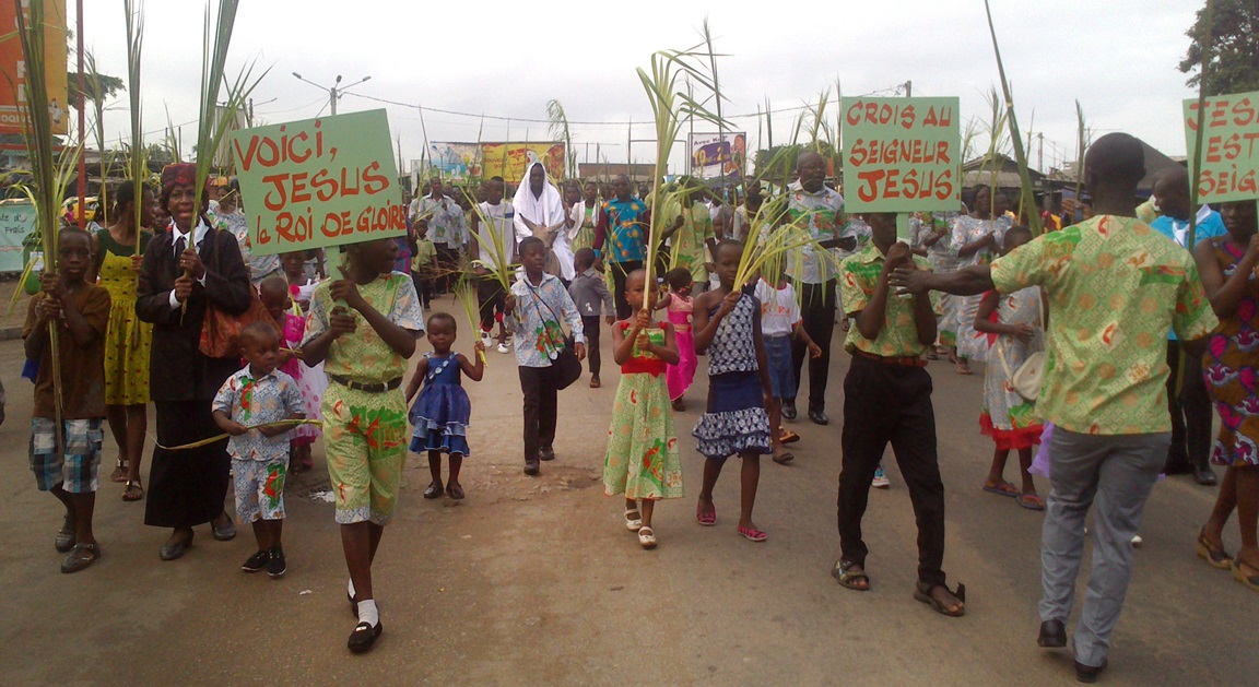 Una multitud marcha agitando palmas por las calles de Port-Bouët, Costa de Marfil, el Domingo de Ramos del 2015. Un hombre representa a Jesucristo montado en un pollino. Esta escena jubilosa es repetida por todo el país por metodistas unidos y católicos marfileños