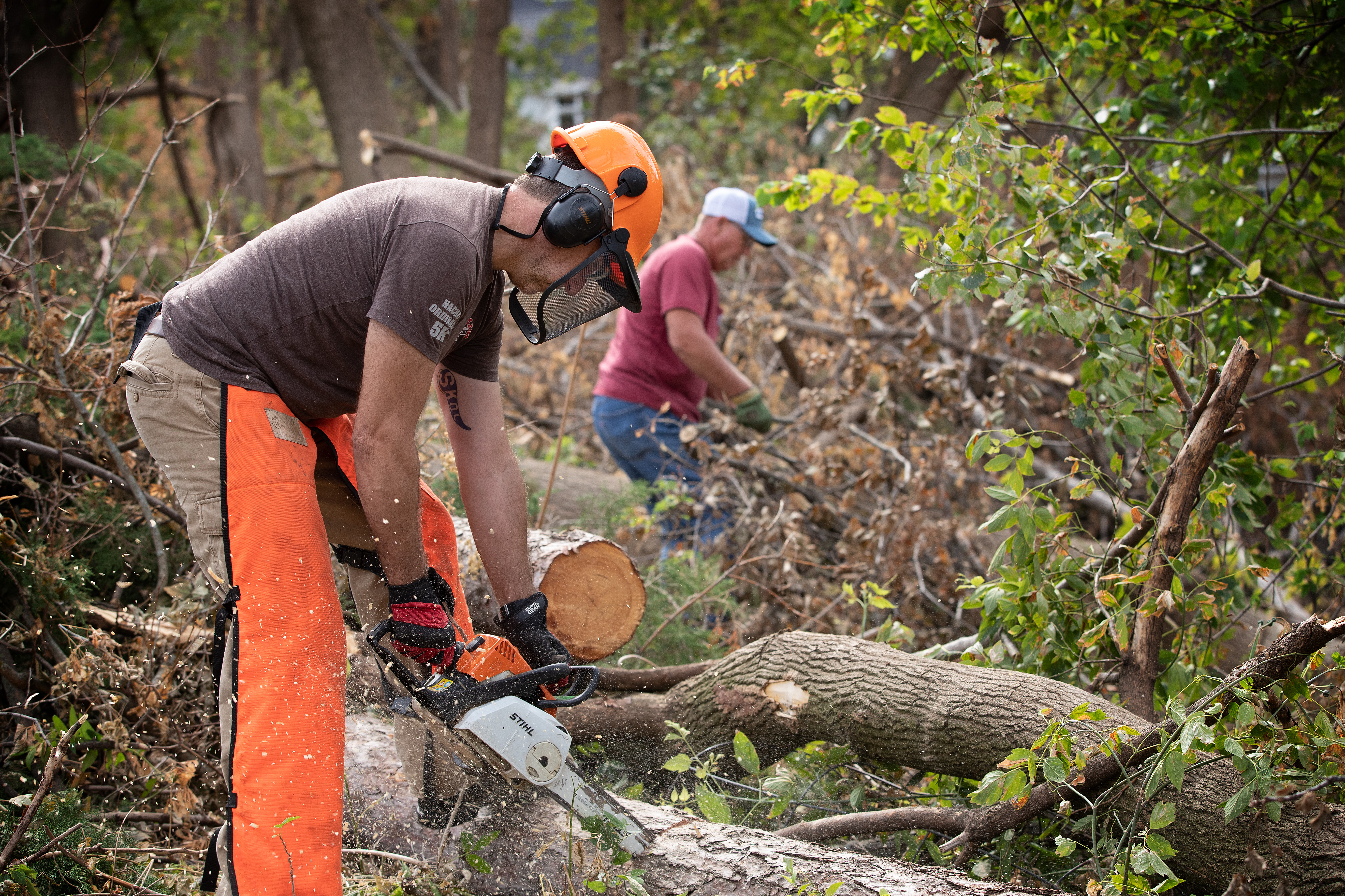 Los voluntarios metodistas unidos Darren Garrett (frente) y Dale Krohn usan motosierras para despejar los árboles caídos en una casa de Cedar Rapids, Iowa, después del derecho que azotó la ciudad en agosto del 2020. Foto por Mike DuBose, UM News.
