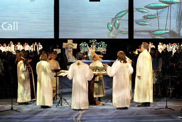 Bishops from the US and central conferences stand around the circular communion table of General Conference to lead those gathered in the Great Thanksgiving.