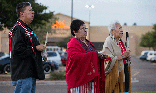 Bishop David Wilson (left) and the Rev. Donna Pewo (center) of The United Methodist Church’s Oklahoma Indian Missionary Conference join with Native American scholar Henrietta Mann in a prayer service for immigrant children held at the Casa Padre detention center, visible behind them, in Brownsville, Texas, in 2018. File photo by Mike DuBose, UM News.