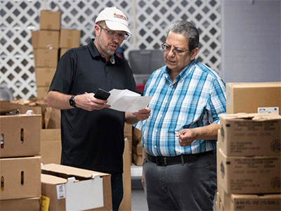 The Revs. Alex Shanks (left) and Juan Ramos discuss recovery efforts following Hurricane Ian while standing among boxes of relief supplies at Time United Methodist Church in Fort Myers, Florida. (Photo: Mike DuBose, UM News)