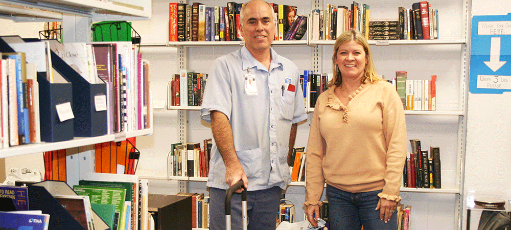 Shannon Wadlington (right) stands with mail carrier Rick Crocker amid shelves of books. Canterbury United Methodist Church in Birmingham, Ala., provides reading materials for inmate populations nationwide. Photo courtesy of the North Alabama Conference.