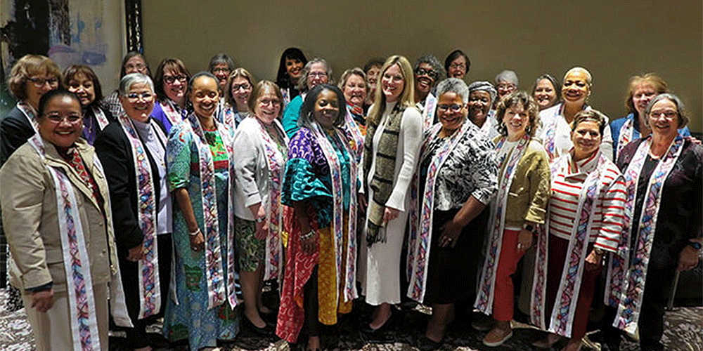 The Rev. Stephanie York Arnold (center), the new top executive of the United Methodist Commission on the Status and Role of Women, stands with 26 active and retired women bishops. York Arnold presented the bishops with stoles made by her mother. “I hope you will wear these when you serve communion, when you open the table wide for all to come and feast on the grace of our Savior,” York Arnold told the bishops. Photo by Heather Hahn, UM News.