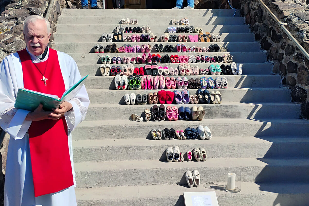 El Rev. Bob Anders a la izquierda, dirigió un momento de oración el 3 de abril que fue Viernes Santo,  en la Iglesia Metodista Unida de la Comunidad de Cedaredge, en Cedaredge, Colorado. La iglesia exhibió en sus escalinatas un memorial compuesto por pares de zapatos, con el fin de representar a las 168 niñas y maestros/as que perdieron la vida el 28 de febrero durante el bombardeo a la escuela de niñas en Minab, Irán. Las fotografías del memorial se hicieron virales en las redes sociales y en medio del frágil alto el fuego, el pueblo metodista unido continúa alzando su voz en contra de la guerra y, en particular, de las amenazas de genocidio. Fotografía cortesía de Anders, Iglesia Metodista Unida de la Comunidad de Cedaredge.