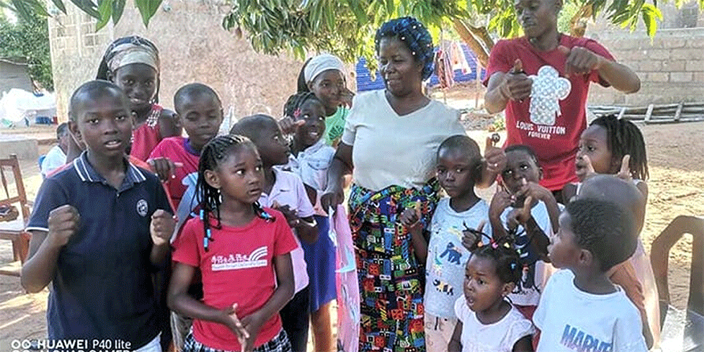 The Rev. Maria Matsinhe, a nurse and health coordinator for The United Methodist Church in Mozambique, interacts with children, including twins Paulo and Joana Buque (pictured at left), at Chucunja Elementary School in Morrumbene village. Matsinhe heads the church’s mobile clinic, which set up at the school to conduct health screenings. Photo by Antonio Wilson, UM News.