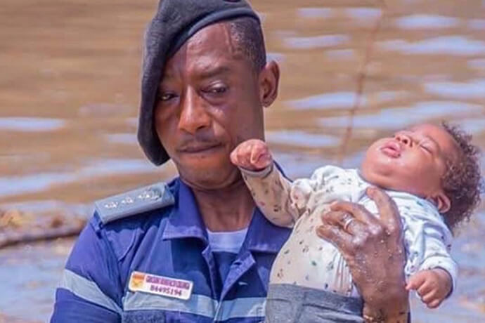 Oficial do Serviço de Protecção Civil e Bombeiros de Angola resgatando uma criança durante as cheias no Rio Cavaco em Benguela. Mais de 1.600 pessoas foram resgatadas com o apoio da Força Aérea, Marinha de Guerra e dos Bombeiros. A criança resgatada recebeu assistência médica no Hospital Geral de Benguela. Foto cortesia da Administração de Benguela, Angola. Notícias MU. 